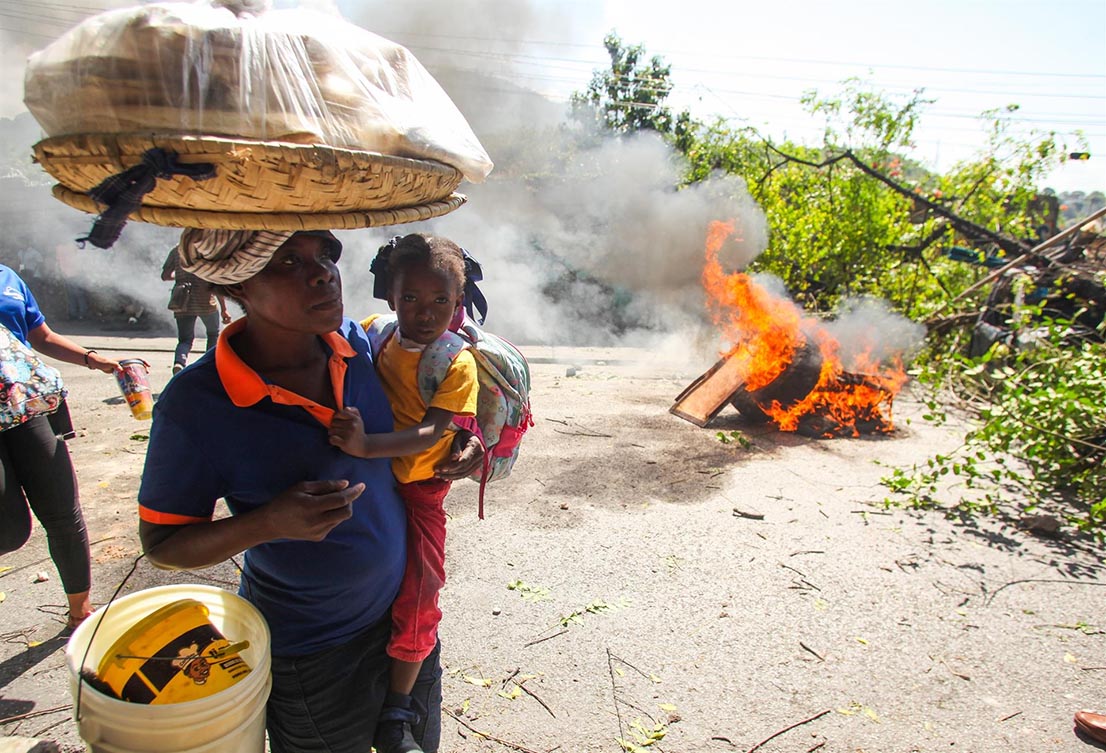 Una mujer con una niña pasan junto a una barricada en llamas, en Puerto Príncipe. - Patrice Noel/ZUMA Press Wire/dpa